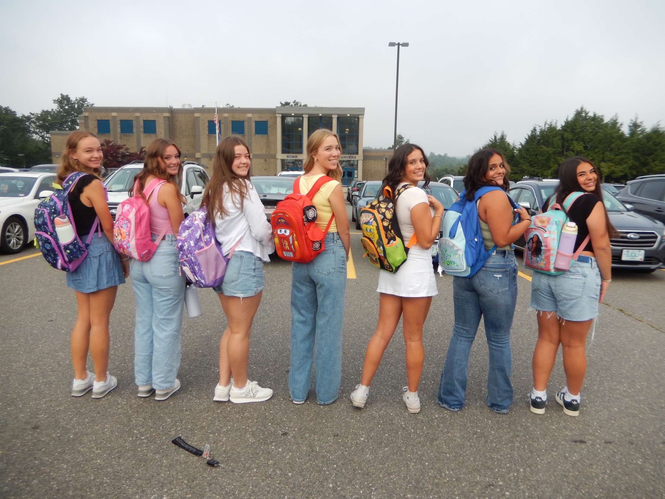 Senior girls looking back with bright smiles, sporting their throwback backpacks. As they head in for their last first day of high school! 