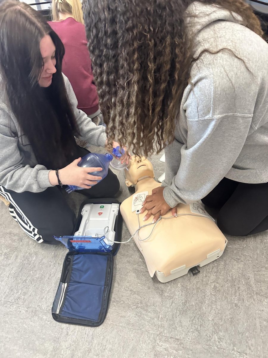 Juniors Maddie Sullivan and Alani Espinal practice using an AED in their Health and Human Services class at Alvirne High School.
